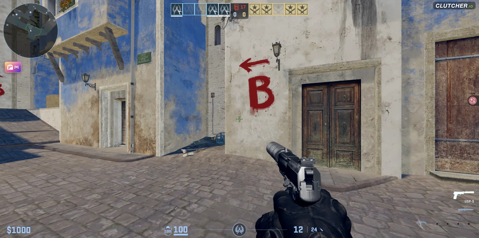 First-person view of Clutcher io on Oasis, with blue and white buildings and a painted B-site direction marker